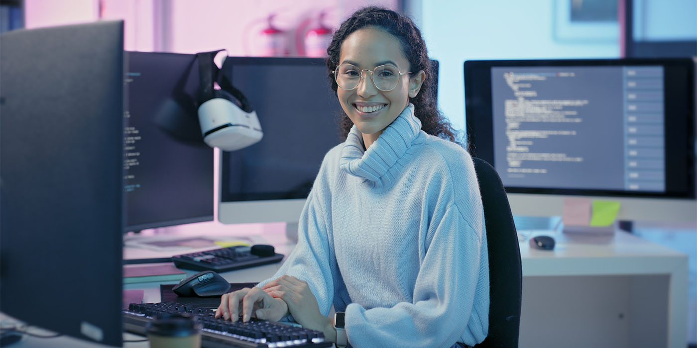 jeune femme souriante à un poste de travail comportant plusieurs écrans d'ordinateurs